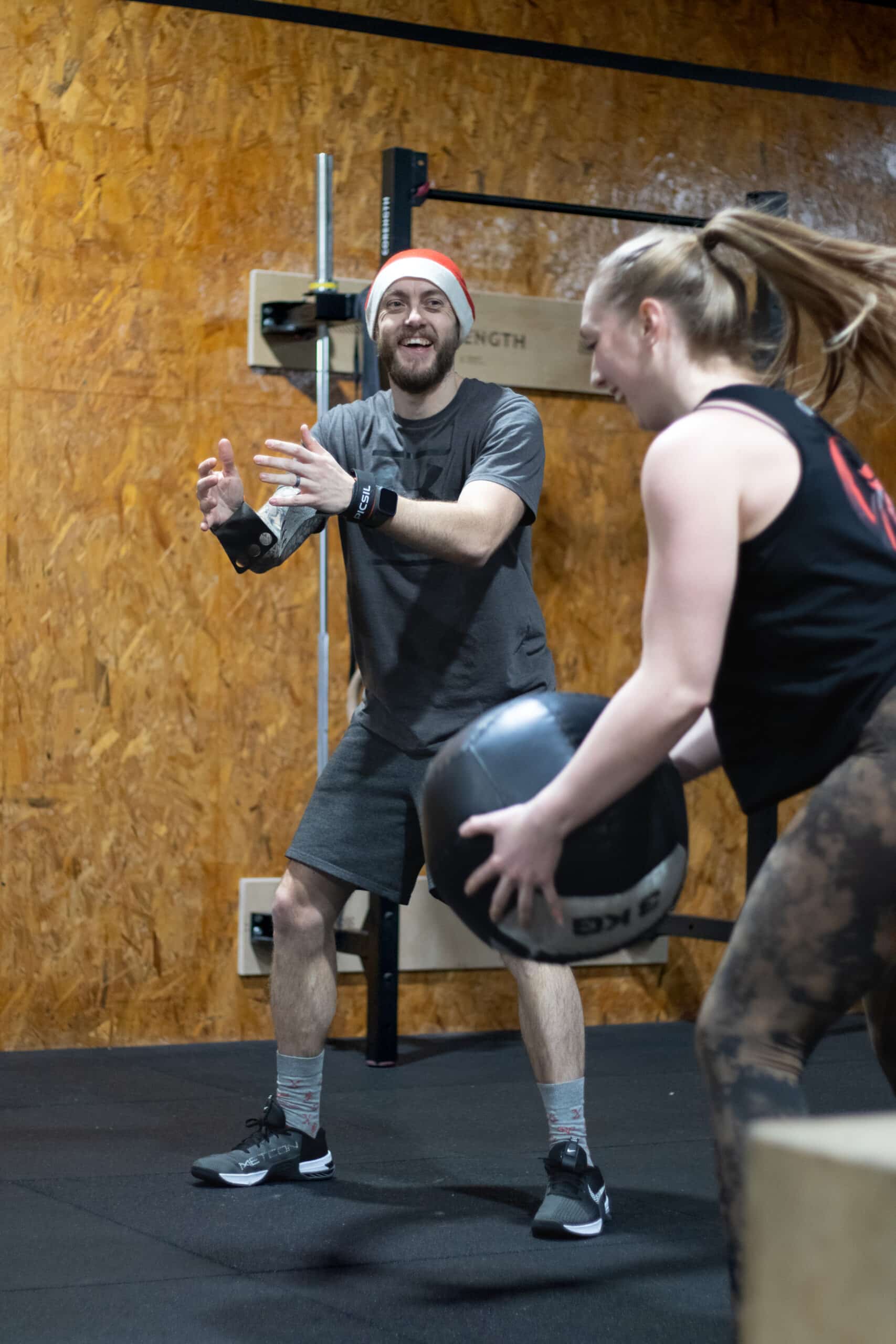 deux adhérents souriant execute un exercice avec un ballon médicinal dans la box CrossFit.