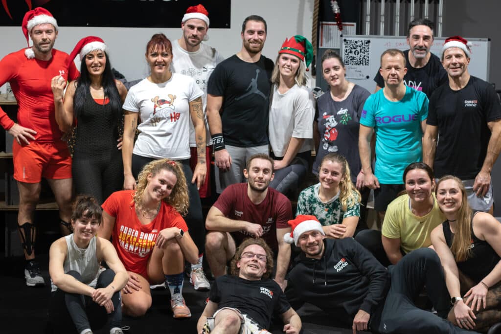 Un groupe joyeux de crossfitters posant ensemble pour une photo dans la box CrossFit Histìa, certains coiffés de bonnets de Noël, symbolisant l'esprit communautaire et festif qui règne dans la salle d'entraînement